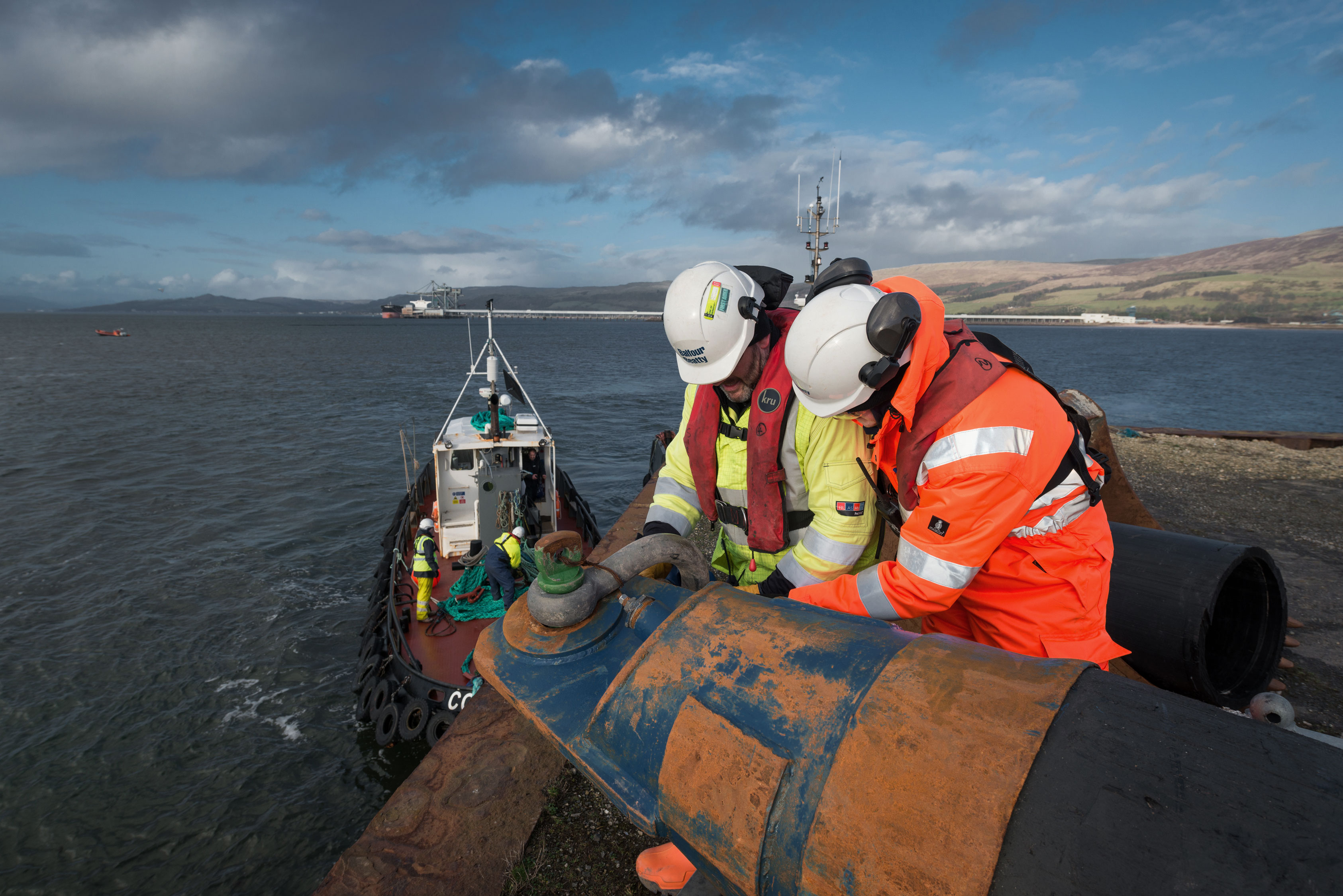 Men in hard hats working on laying pipes by sea, hunterston, scotland