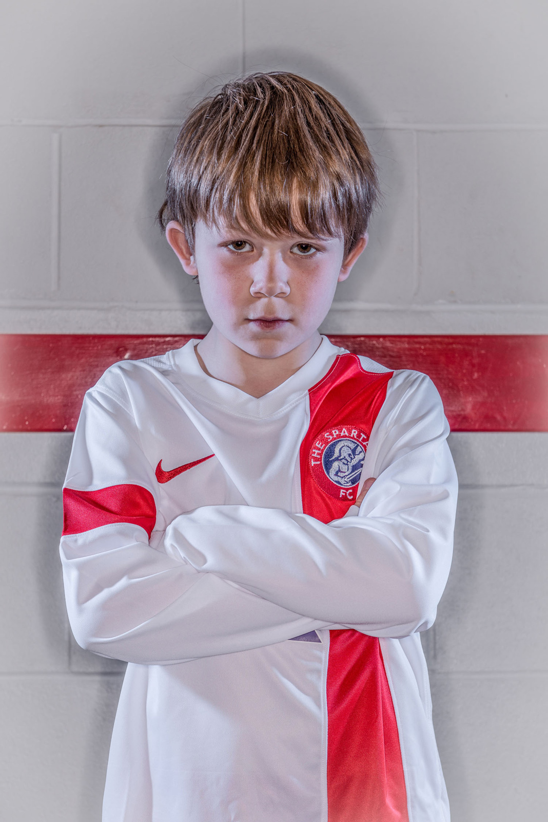 Portrait of young boy in football kit standing in changing rooms staring at camera