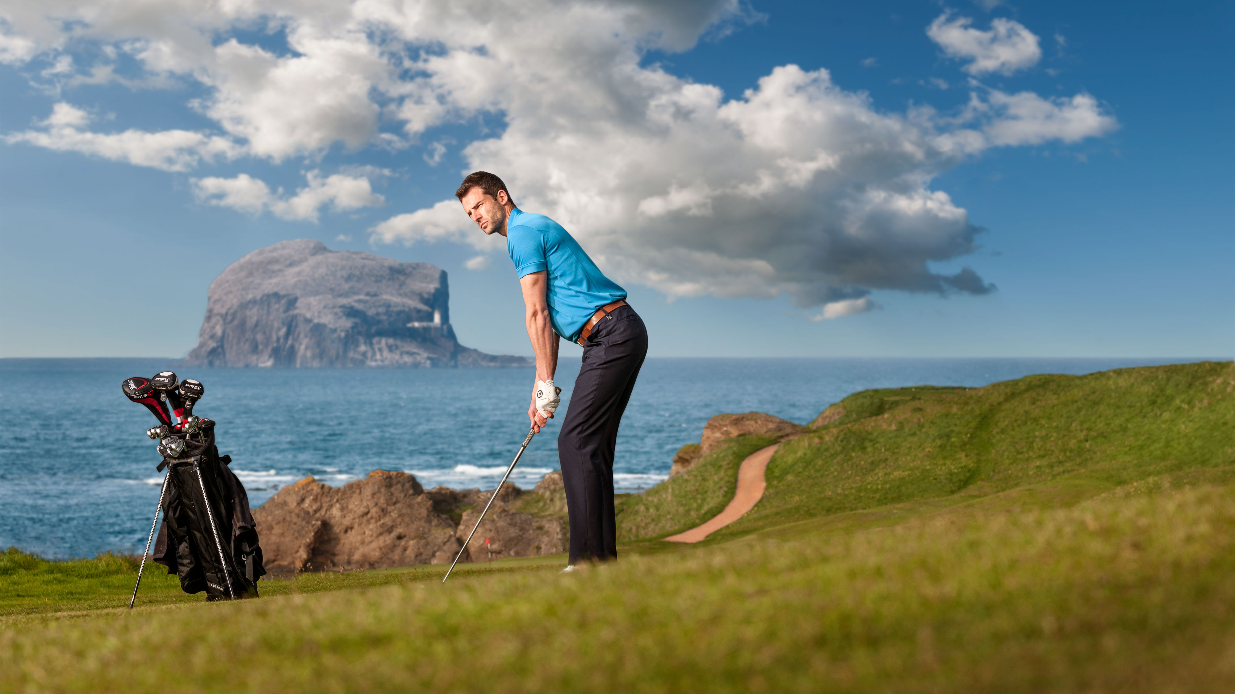 Man golfing by sea in Scotland on beautiful sunny day with Bass rock